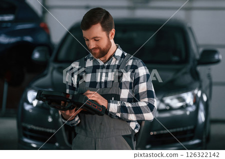 Holding tablet. Man in uniform is working in the auto salon Holding tablet. Man in uniform is working in the auto salon 126322142