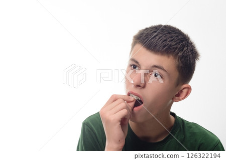 Teenage boy adjusting his braces, looking thoughtful against a white background. Teenage boy adjusting his braces, looking thoughtful against a white background. 126322194