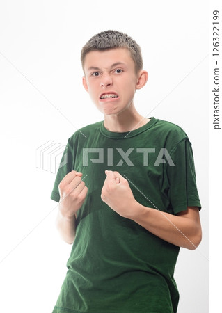 Angry teenage boy clenching fists, wearing a green shirt. Studio shot against a white background. 126322199