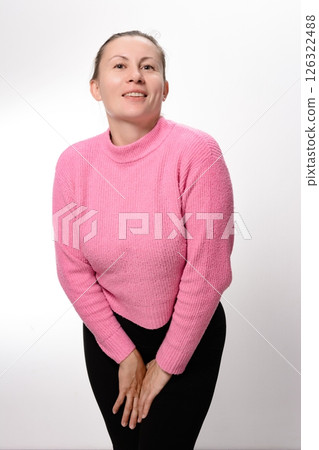 Woman in pink sweater and black pants holding herself, looking at the camera. 126322488