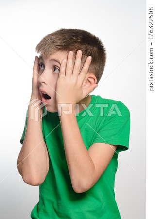 Surprised boy in green shirt. Hands on face, looking shocked. Youthful expression of amazement. Surprised boy in green shirt. Hands on face, looking shocked. Youthful expression of amazement. 126322508