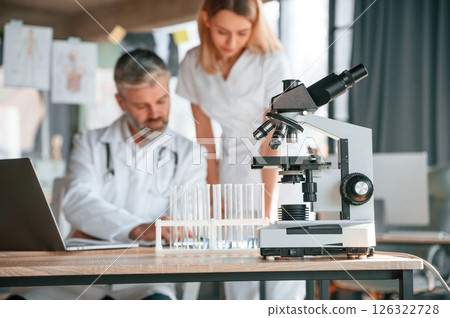 Laptop, test tubes, microscope. Two clinic workers are indoors together. Senior man with young woman 126322728