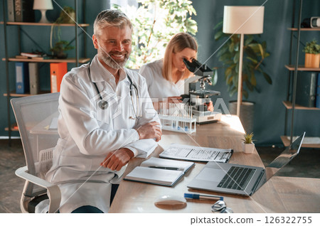 Man is smiling, woman is using microscope. Two clinic workers are indoors together 126322755