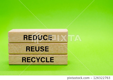 Wooden blocks with Reduce, Reuse and Recycle text placed on green surface. Symbolizing commitment to eco friendly habits and waste reduction 126322763