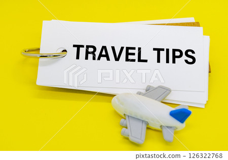 Travel Tips text on white notepad with toy airplane on yellow cover background. Away from office concept Travel Tips text on white notepad with toy airplane on yellow cover background. Away from office concept 126322768