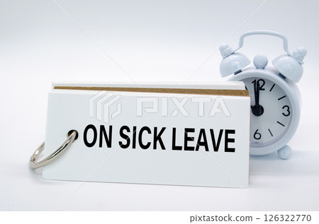 One Sick Leave text on white notepad with alarm clock on white background. Away from office concept One Sick Leave text on white notepad with alarm clock on white background. Away from office concept 126322770