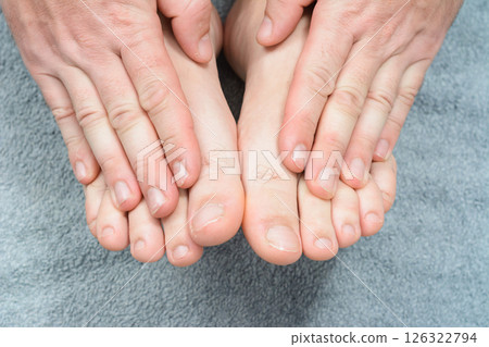 Close-up of hands holding feet on a soft gray surface. Close-up of hands holding feet on a soft gray surface. 126322794