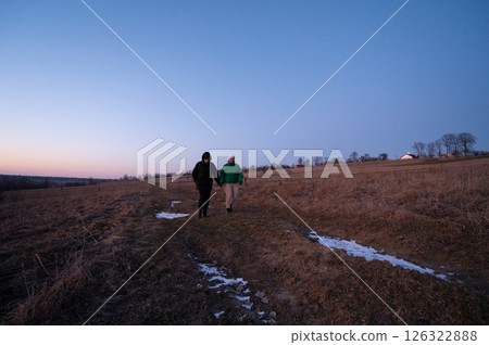 Couples stroll across a serene meadow at dusk, hand in hand, as the soft glow of twilight embraces the quiet landscape in winter 126322888