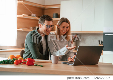 Sitting, using laptop. Young couple is on the kitchen together 126322996