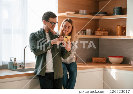 Man showing some media to woman on the phone. Young couple is on the kitchen together Man showing some media to woman on the phone. Young couple is on the kitchen together 126323017