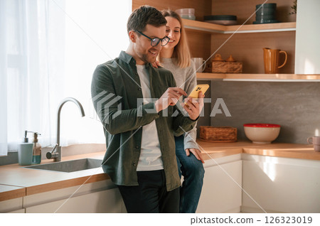 Man showing some media to woman on the phone. Young couple is on the kitchen together 126323019