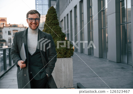 Smiling, feeling good. Handsome man in formal clothes is outdoor near the business building Smiling, feeling good. Handsome man in formal clothes is outdoor near the business building 126323467