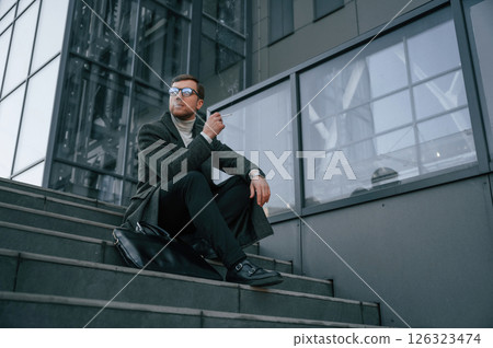 Sitting on the stairs and smoking. Handsome man in formal clothes is outdoor near the business building Sitting on the stairs and smoking. Handsome man in formal clothes is outdoor near the business building 126323474