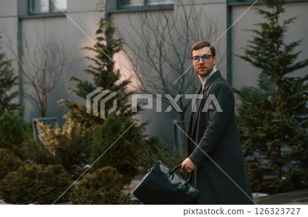 Walking near the fir trees. Handsome man in formal clothes is outdoor 126323727