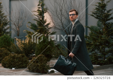 Walking near the fir trees. Handsome man in formal clothes is outdoor 126323728