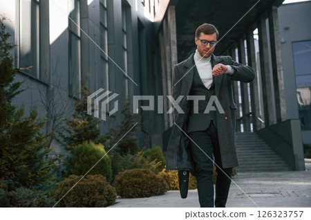 Checking the time. Handsome man in formal clothes is outdoor near the business building Checking the time. Handsome man in formal clothes is outdoor near the business building 126323757