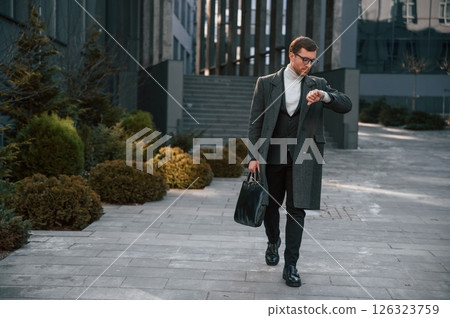 Checking the time. Handsome man in formal clothes is outdoor near the business building 126323759