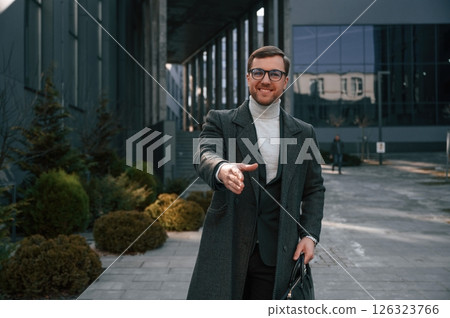 Greetings, giving hand to shake. Handsome man in formal clothes is outdoor near the business building 126323766