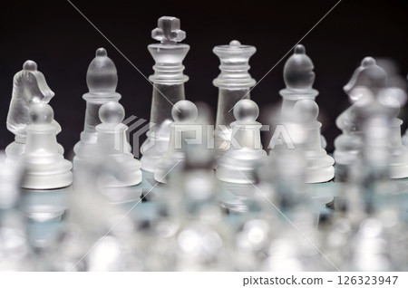 glass, transparent chess pieces on a checkerboard, selective focus, close-up, isolated on black 126323947