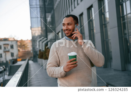 Having a phone call. Handsome black man is outdoors near the business building 126324285