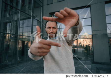 Making photo gesture. Handsome black man is outdoors near the business building 126324294