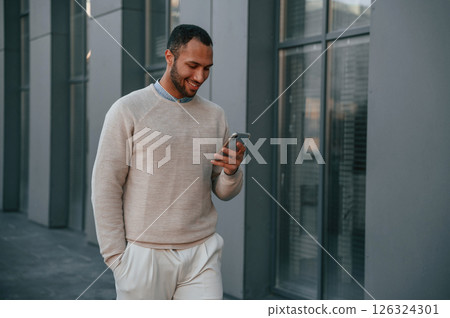 Against modern business building. With smarpthone. Handsome black man is outdoors 126324301