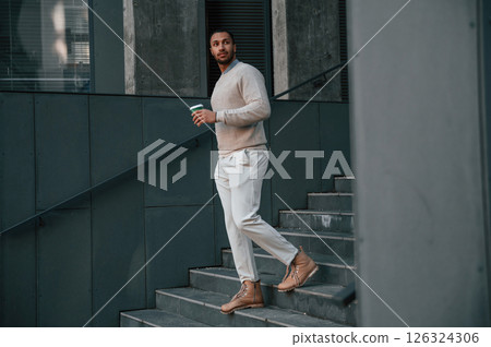 Drink in hand. Handsome black man is outdoors near the business building 126324306