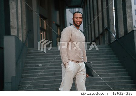 Smiling and holding laptop. Handsome black man is outdoors near the business building Smiling and holding laptop. Handsome black man is outdoors near the business building 126324353