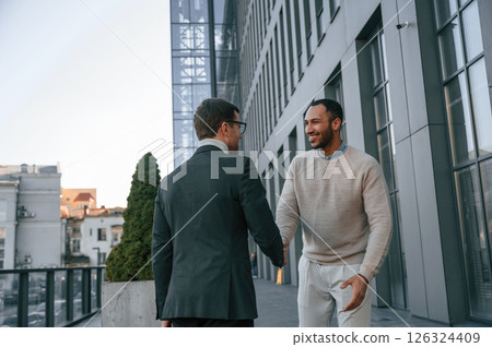 Conception of collaboration. Businessman in formal clothes is with black man outdoors in the city Conception of collaboration. Businessman in formal clothes is with black man outdoors in the city 126324409
