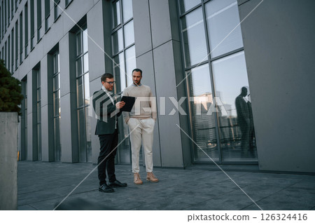 With notepat and documents. Businessman in formal clothes is with black man outdoors in the city 126324416