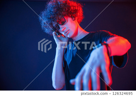 DJ is in the club. Young man with curly hair is indoors illuminated by neon lighting 126324695