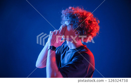 Young man with curly hair is indoors illuminated by neon lighting Young man with curly hair is indoors illuminated by neon lighting 126324738