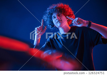 Dj is playing music from vinyl. Young man with curly hair is indoors illuminated by neon lighting 126324751