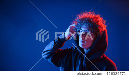 Wearing the hood. Young man with curly hair is indoors illuminated by neon lighting 126324771