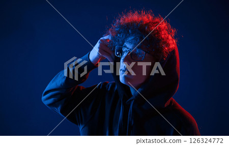 Wearing the hood. Young man with curly hair is indoors illuminated by neon lighting 126324772