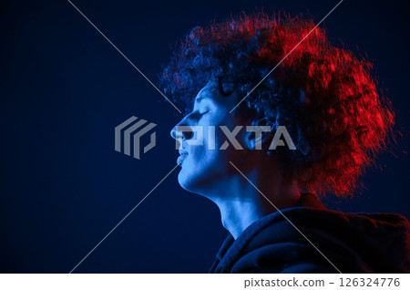 View from the side. Young man with curly hair is indoors illuminated by neon lighting 126324776