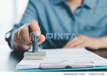 Businessman hands stamp approve on financial business approval document paper. Man hand accepted permit contract agreement. Broker manager sign contract bank guarantee approved stamp application form Businessman hands stamp approve on financial business approval document paper. Man hand accepted permit contract agreement. Broker manager sign contract bank guarantee approved stamp application form 126325289