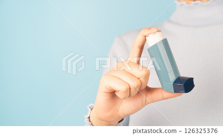 Woman using asthma inhaler for relief asthma attack over light blue background. Pharmaceutical products is used to prevent and treat wheezing and shortness of breath caused asthma or COPD. Close up. 126325376