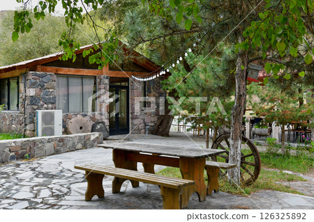 Scenic Outdoor Dining Area Next to Cozy Stone Cottage Surrounded by Trees in Nature Scenic Outdoor Dining Area Next to Cozy Stone Cottage Surrounded by Trees in Nature 126325892
