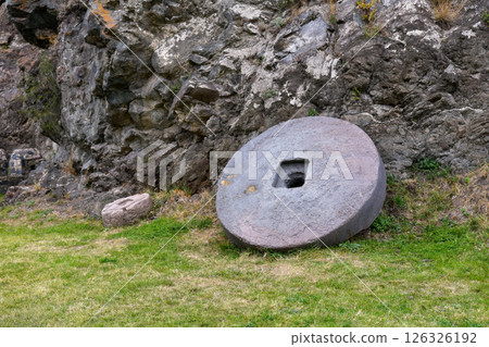 Ancient Stone Wheel and Smaller Artifact Beside Rocky Outcrop in Historical Site 126326192