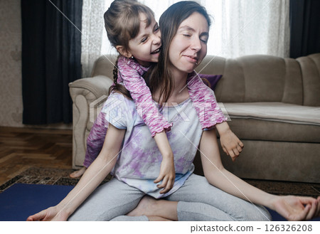 Young mother tries to meditate and do a home workout while her playful daughter gets in her way. Interrupted yoga at home and parenting reality. Mom and daughter having fun Young mother tries to meditate and do a home workout while her playful daughter gets in her way. Interrupted yoga at home and parenting reality. Mom and daughter having fun 126326208