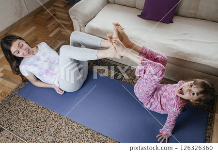 Mom and daughter doing yoga and meditation at home. Home workout together. Fun and active family time 126326360