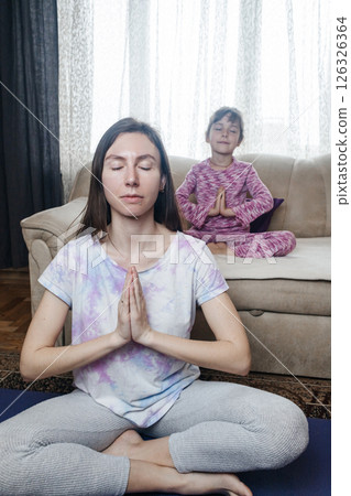 Mom and daughter doing yoga and meditation at home. Home workout together. Fun and active family time 126326364