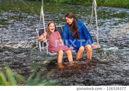a woman and a young girl are swinging across a fast-flowing river, laughing and splashing with water a woman and a young girl are swinging across a fast-flowing river, laughing and splashing with water 126326377