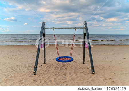 Colorful swing set on a sandy beach near calm waves under a partly cloudy sky during sunset Colorful swing set on a sandy beach near calm waves under a partly cloudy sky during sunset 126326429