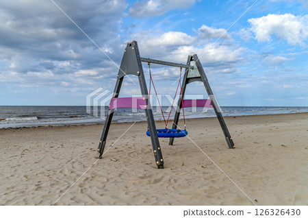 Colorful swing set on a sandy beach near calm waves under a partly cloudy sky during sunset 126326430