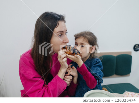 Mother and daughter in a cafe, drinking coffee and cocoa, eating a croissant and cake. Having fun and enjoying spending time together Mother and daughter in a cafe, drinking coffee and cocoa, eating a croissant and cake. Having fun and enjoying spending time together 126326474