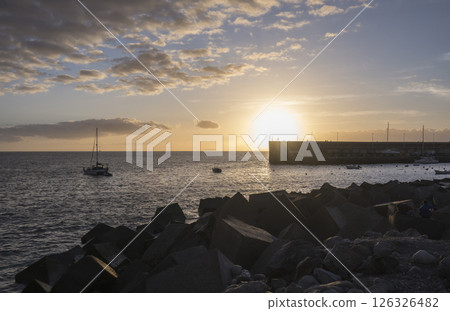 Golden sunset view of Playa de San Juan bay with protected sand beach and small harbor. Playa de San Juan is a small fishing village on the south west of Tenerife island. Golden sunset view of Playa de San Juan bay with protected sand beach and small harbor. Playa de San Juan is a small fishing village on the south west of Tenerife island. 126326482