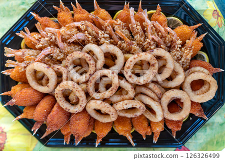 A colorful platter of various fried seafood and appetizers served on a black tray, perfect for gatherings or celebrations A colorful platter of various fried seafood and appetizers served on a black tray, perfect for gatherings or celebrations 126326499