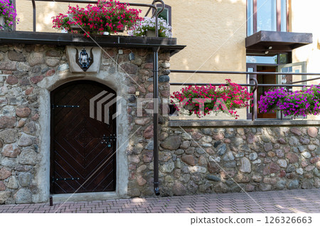 A rustic wooden door is set in a stone wall with colorful flowers hanging above it. A rustic wooden door is set in a stone wall with colorful flowers hanging above it. 126326663